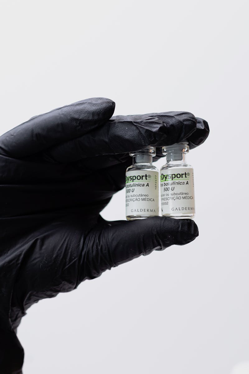 Close-up of black gloved hand holding two Botox vials in a medical setting.